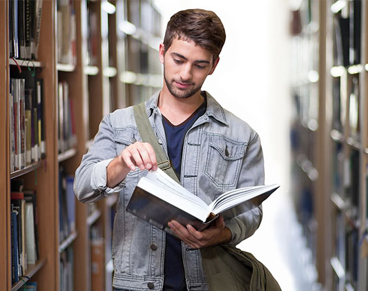 Estudiante latinoamericano con un libro en la biblioteca de la universidad de Madrid, España.